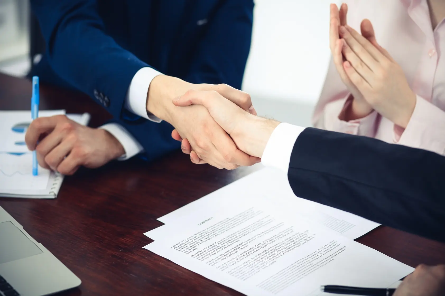 Three people at a conference table. Two of them are shaking hands